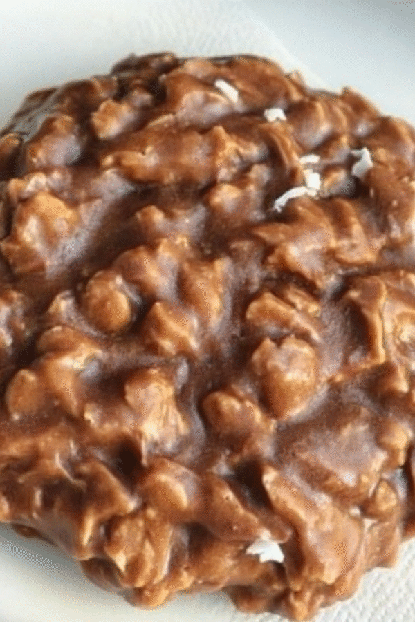 Stack of no-bake keto cookies with chocolate and peanut butter, garnished with chopped nuts on parchment paper showing their rich, fudgy texture