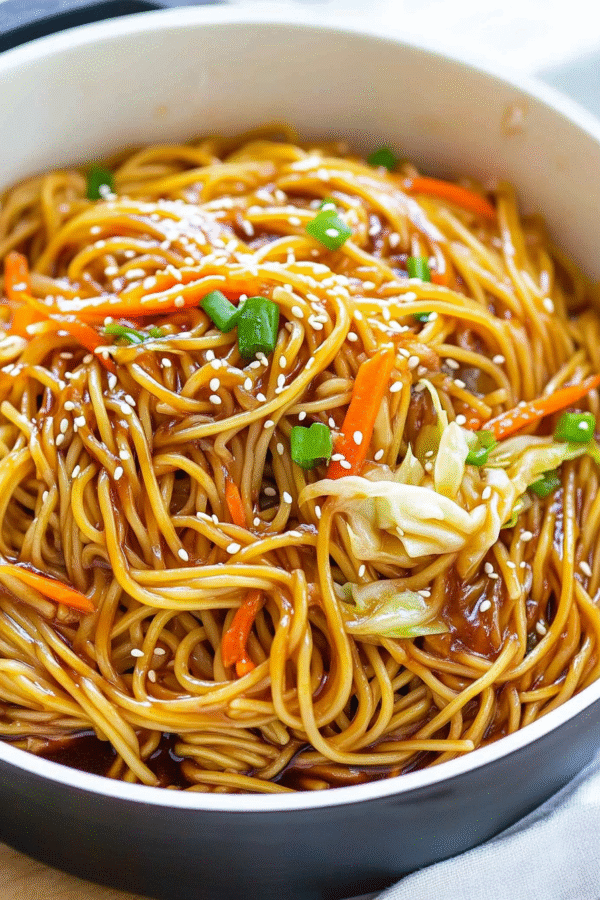 Glossy teriyaki noodles in a large pot with colorful vegetables, garnished with sesame seeds and green onions, showing the rich sauce coating